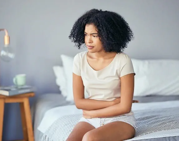 Patient sitting on a bed holding their stomach looking concerned