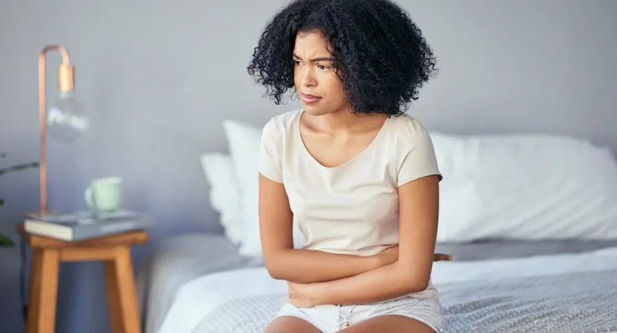 Patiente assise sur un lit, se tenant le ventre d’un air préoccupé