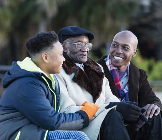 A Black father, son and grandfather sitting in a park. 