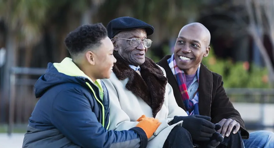 A Black father, son and grandfather sitting in a park.