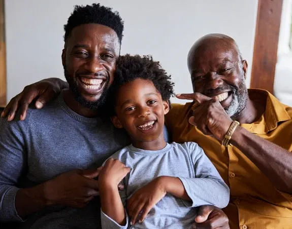 A Black father, son and grandson sitting and smiling.