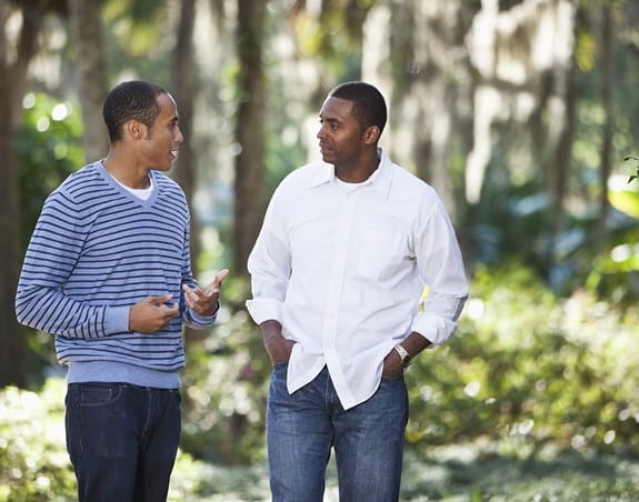 A Black father and son talking and walking in a park.