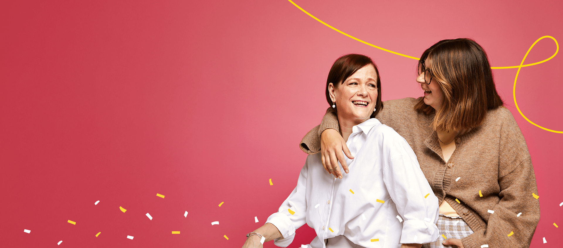 Two women sitting together and smiling at each other, one with an arm around the other.