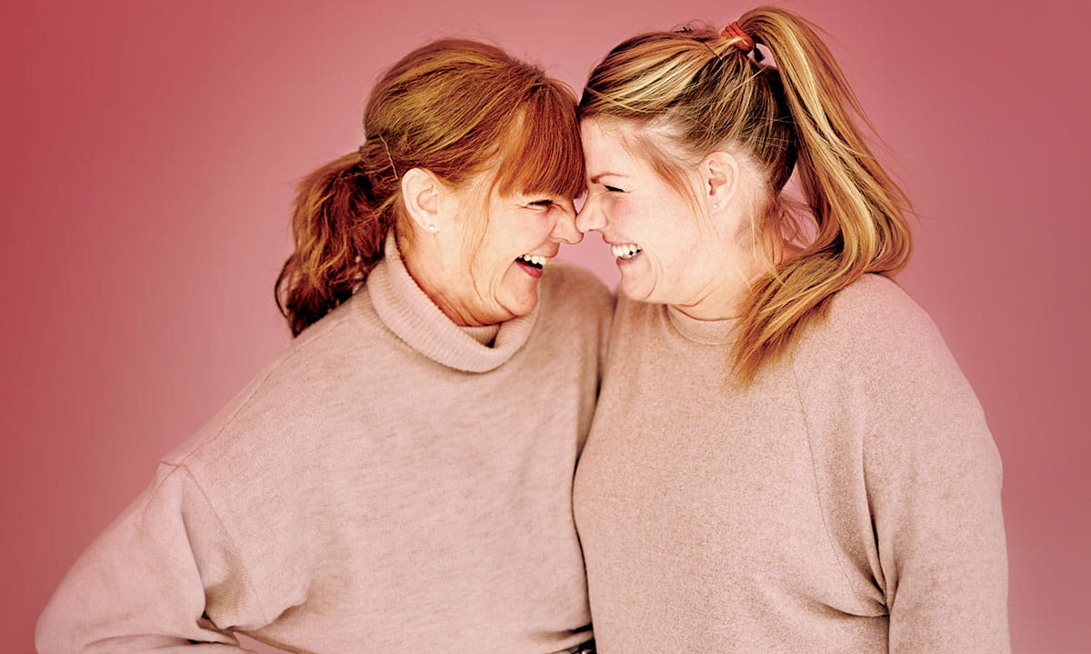 Two women standing close together and leaning their heads toward each other.