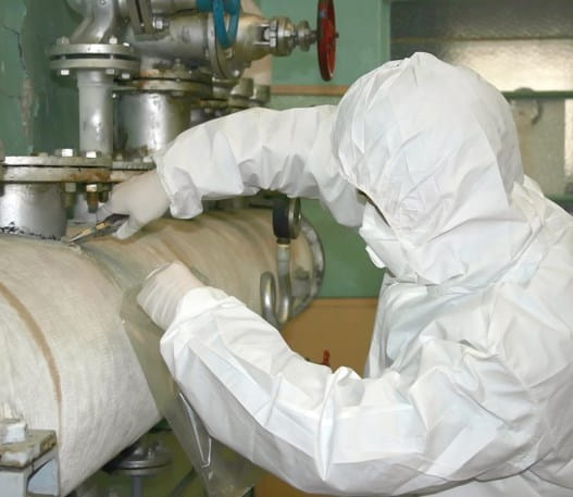 Worker in protective clothing removing asbestos from an old pipe