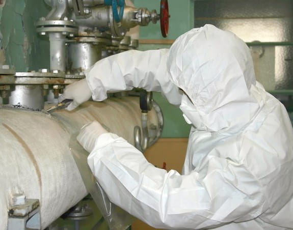 Worker in protective clothing removing asbestos from an old pipe