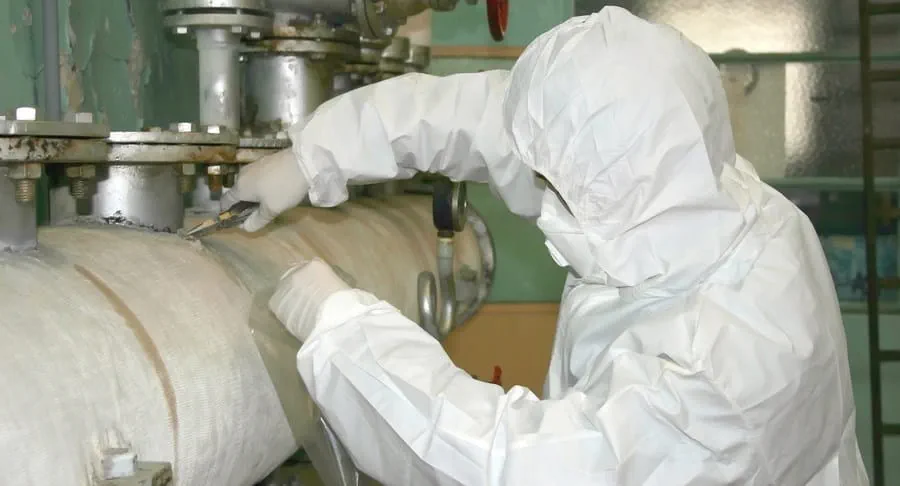 Worker in protective clothing removing asbestos from an old pipe