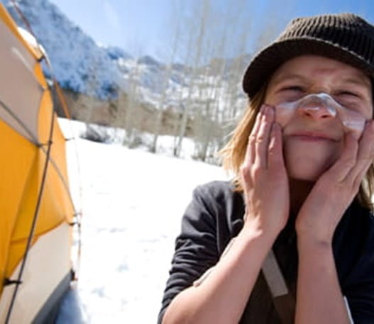 Un enfant sur un site de camping d’hiver, en train d’appliquer un écran solaire