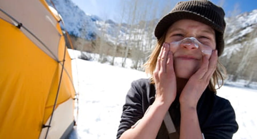Un enfant sur un site de camping d’hiver, en train d’appliquer un écran solaire