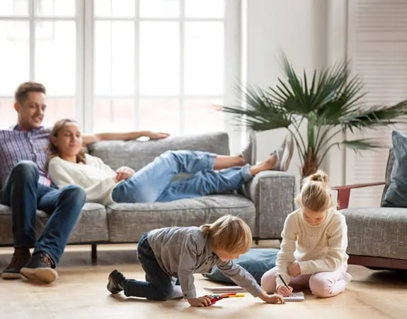 Parents sitting on a couch watching their children play on the floor