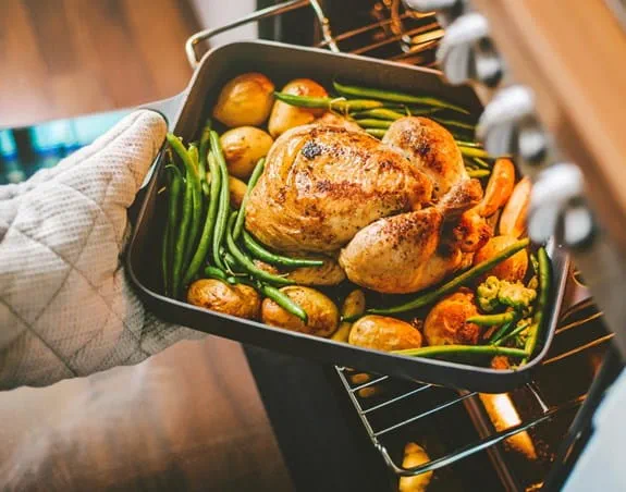 A roasted chicken and veggies being taken out of the oven