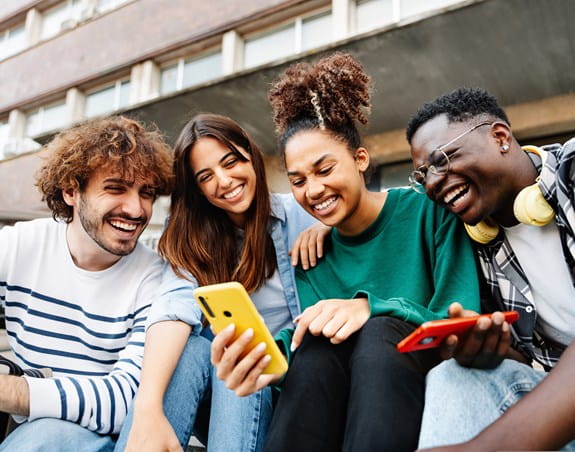 Four young adults laughing together and looking at a cellphone