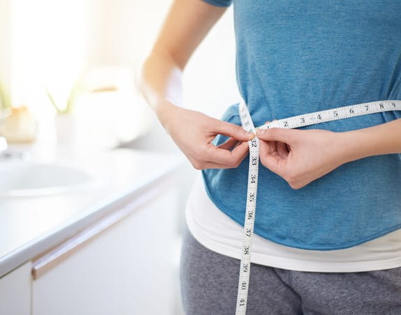 Person measuring their waist size with a measuring tape