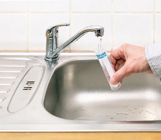 Person testing tap water in their home for arsenic