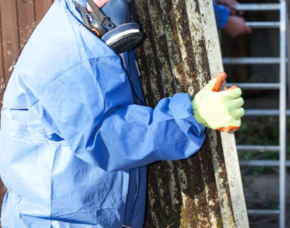 Worker wearing safety gear carrying a panel covered in asbestos