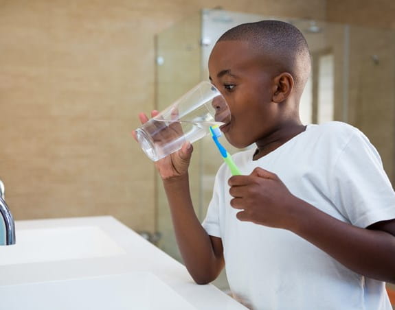 Child rinsing their mouth with tap water after brushing their teeth