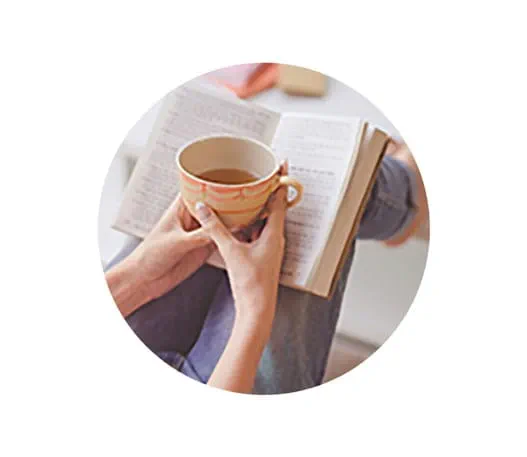 Une personne tenant une tasse de thé tout en lisant un livre