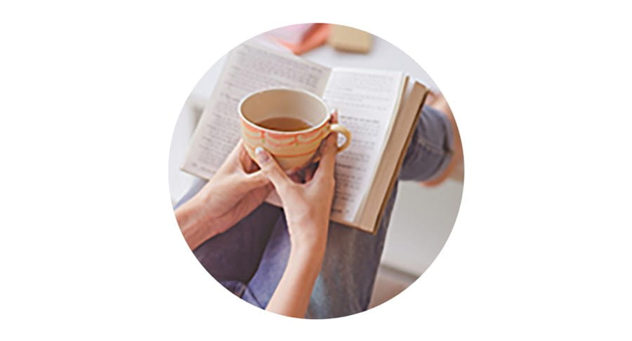 Une personne tenant une tasse de thé tout en lisant un livre