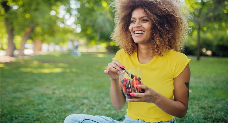 Une personne assise dehors dans l’herbe, mangeant des petits fruits