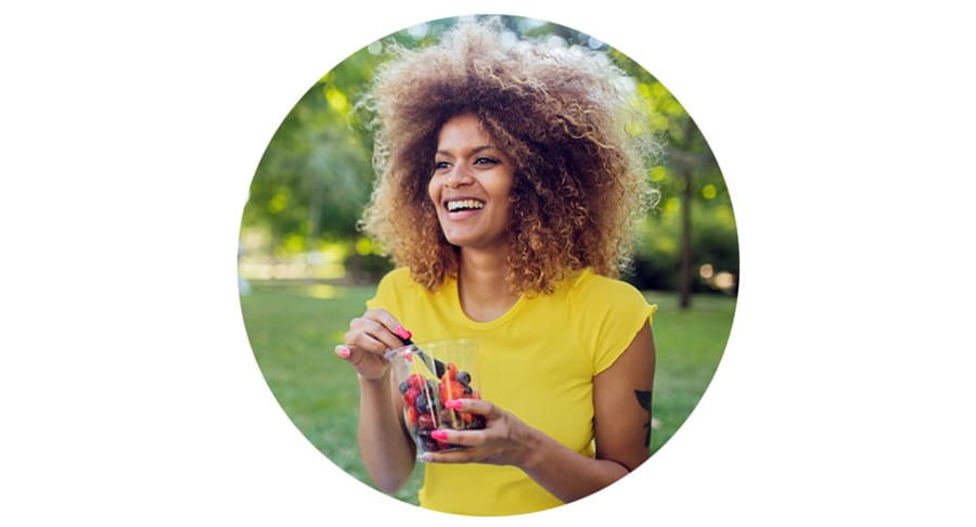 Une personne assise dehors dans l’herbe, mangeant des petits fruits