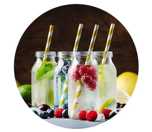 Four mocktails on a table with berries and other fruit