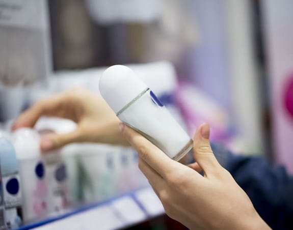 Person choosing between deodorant bottles on a shelf