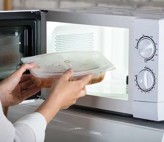 Person putting a container of food into a microwave