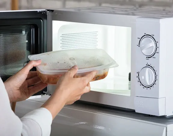 Person putting a container of food into a microwave