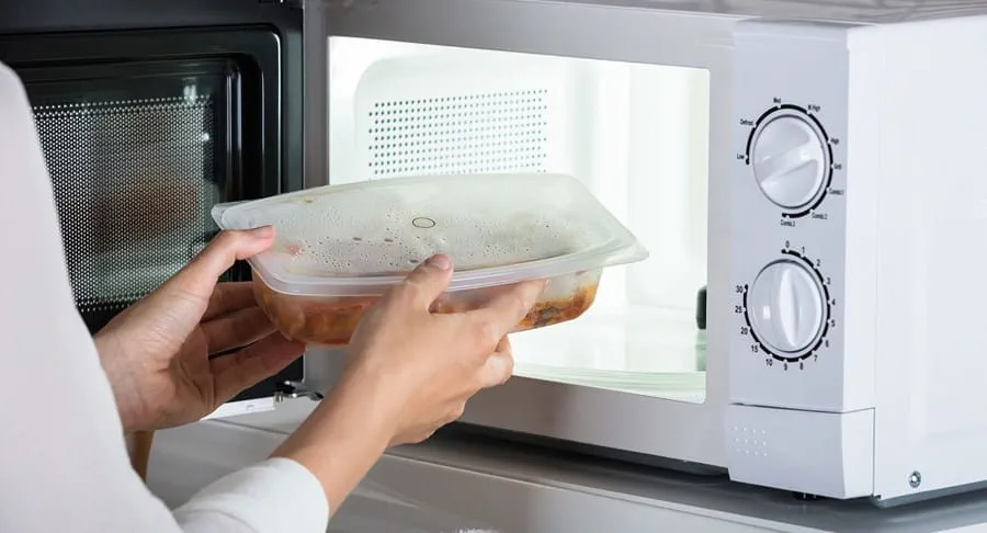 Person putting a container of food into a microwave