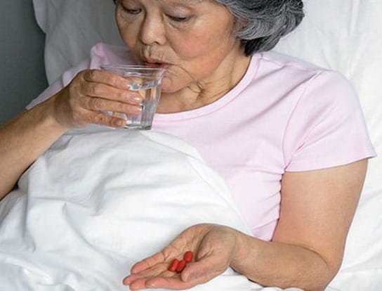 Femme plus âgée assise dans son lit en prenant des médicaments