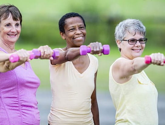 Three women standing next to each other and exercising with dumbbells