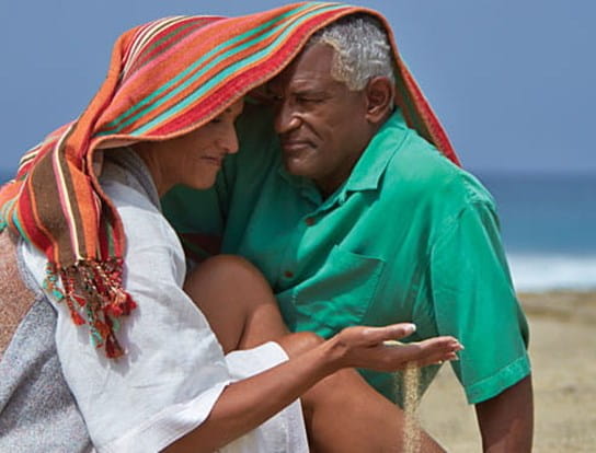 An older couple hugging under a towel at the beach