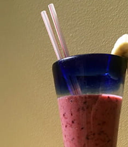 A fruit smoothie with two straws and a slice of banana on the rim of the glass