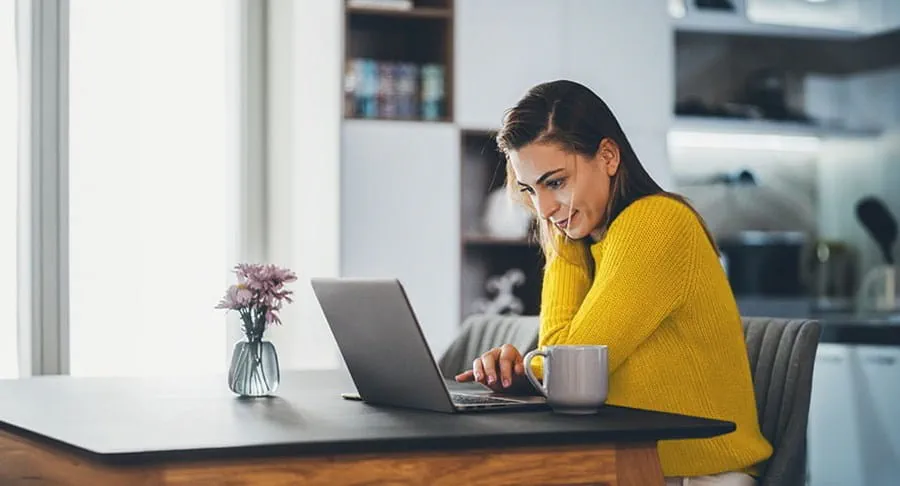 Femme assise à une table de cuisine, travaillant sur un ordinateur portable.