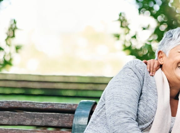 Two grandparents sit on a park bench hugging their granddaughter