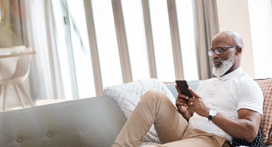 An elderly man sits on his couch looking at his phone