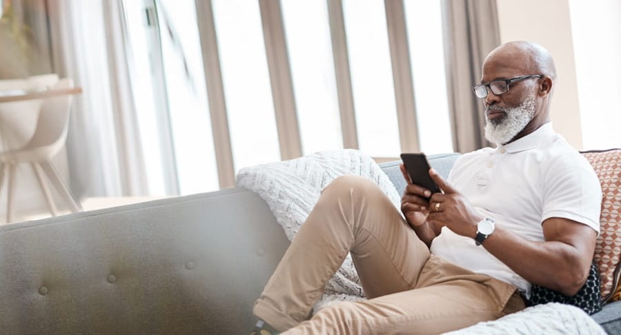 Homme âgé assis dans un canapé, regardant son téléphone.
