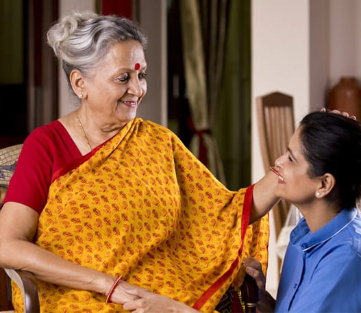 A woman and elderly woman smile while embracing one another