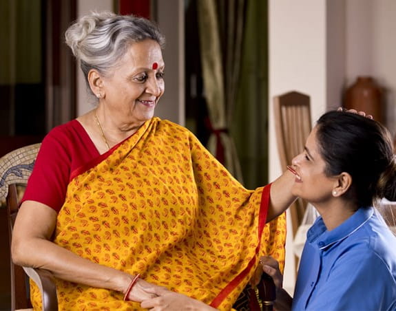 A woman and elderly woman smile while embracing one another