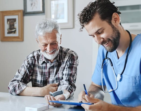 A doctor and his patient are smiling together while the doctor takes notes