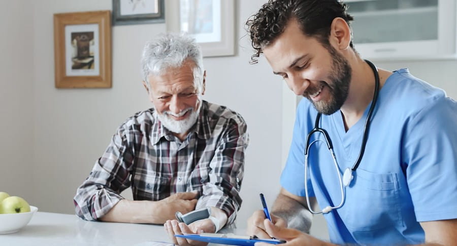 A doctor and his patient are smiling together while the doctor takes notes