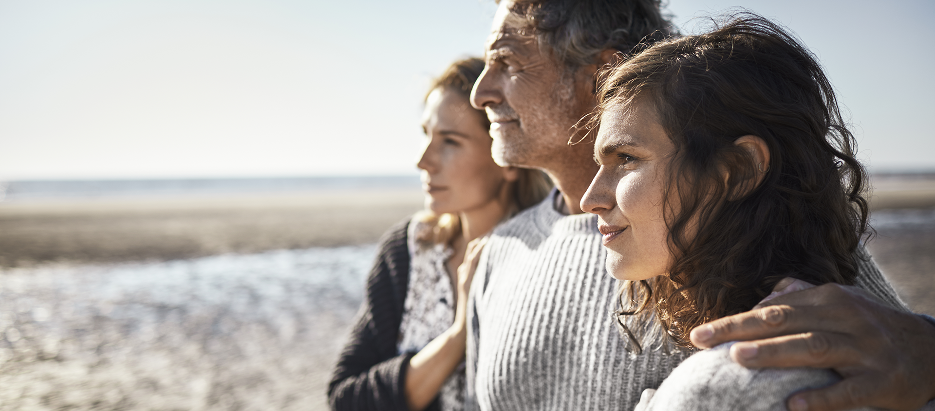 Trois personnes debout sur la plage scrutant l’horizon