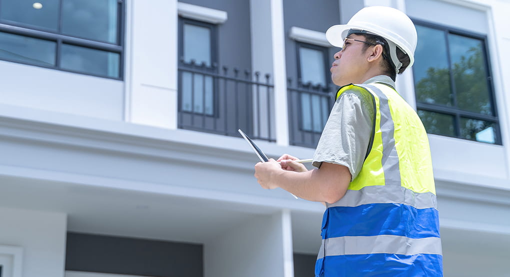 Une personne portant un équipement de sécurité en train d’inspecter l’extérieur d’un bâtiment moderne.