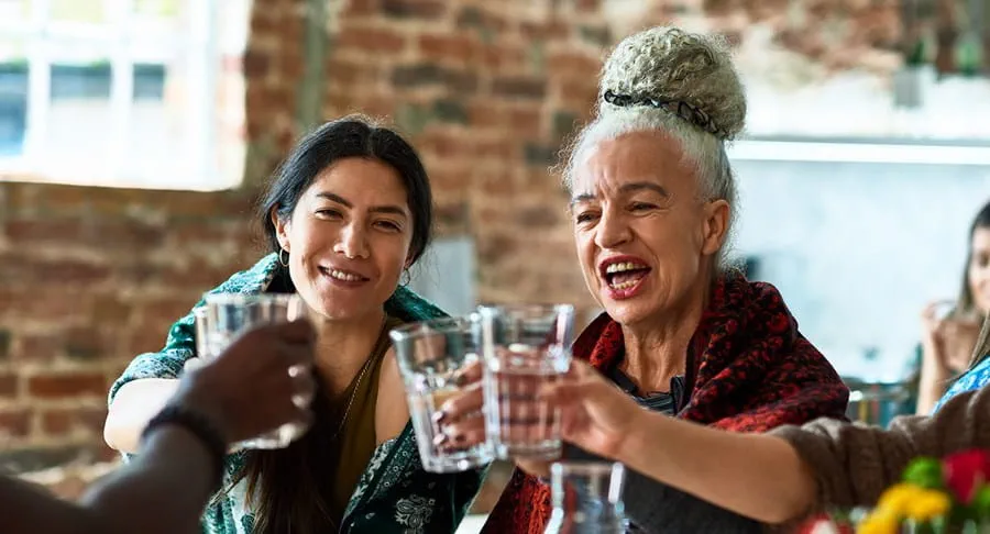 A group of happy women drinking water around a table.