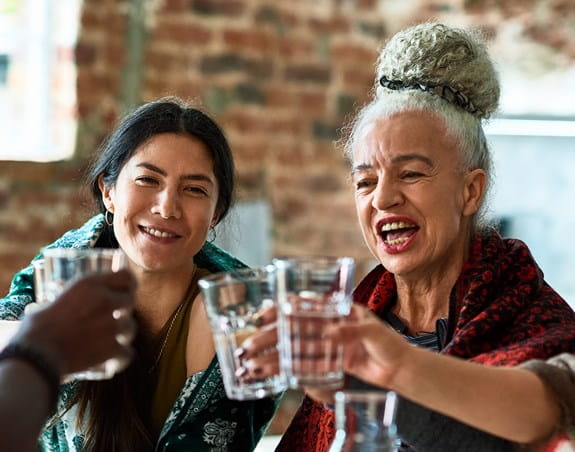 A group of happy women drinking water around a table. 