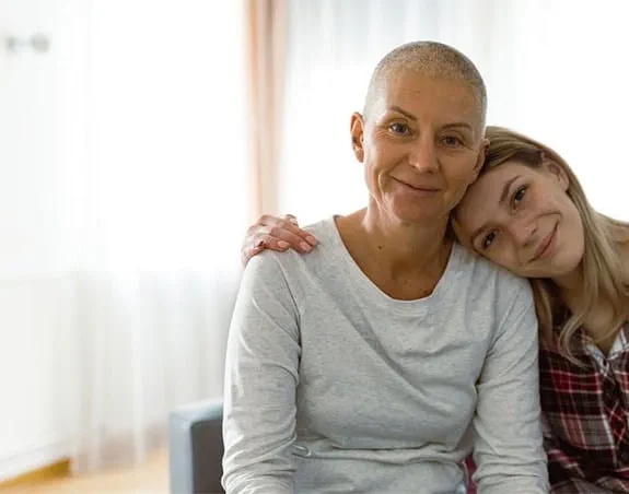 Une femme est assise sur un canapé, les bras autour d'une femme plus âgée. Elles sourient toutes les deux.