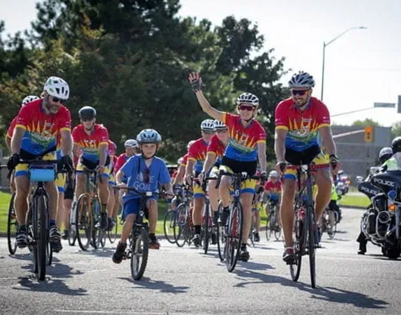 A child on a bicycle leads a group of 10 cyclists wearing matching uniforms
