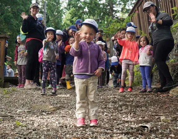 A little girl standing in front of a group with adults and children.