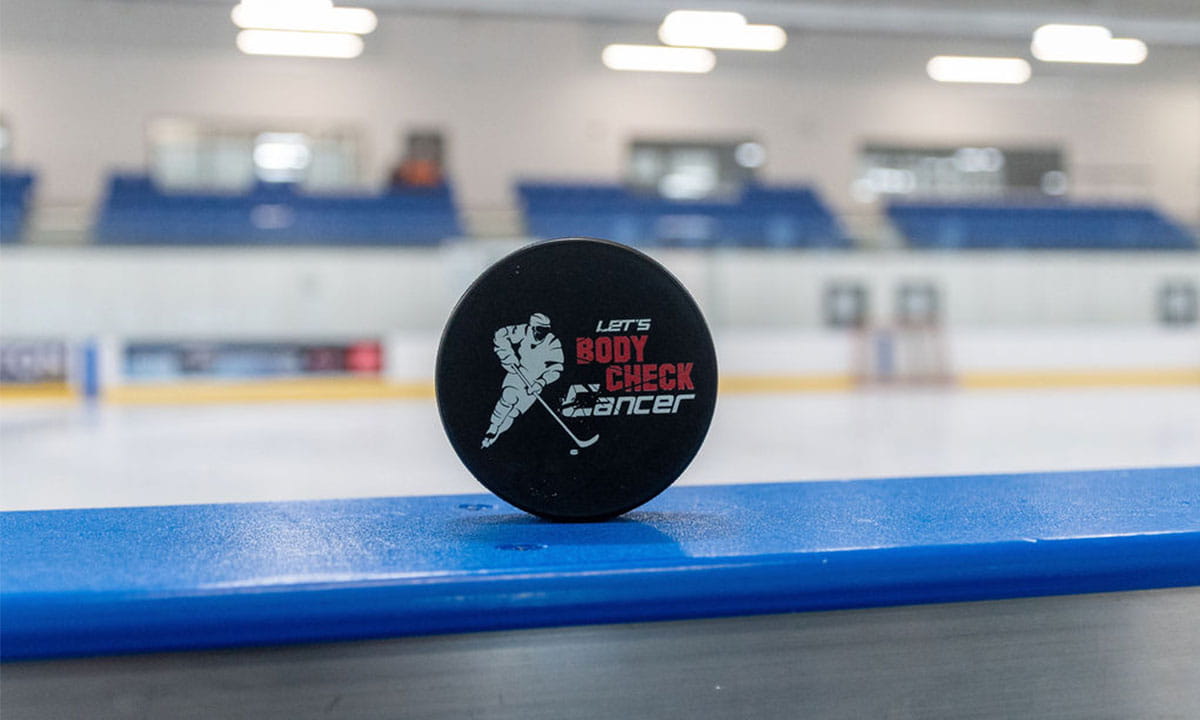 Let’s Body Check Cancer hockey puck sitting on the side of the rink boards.