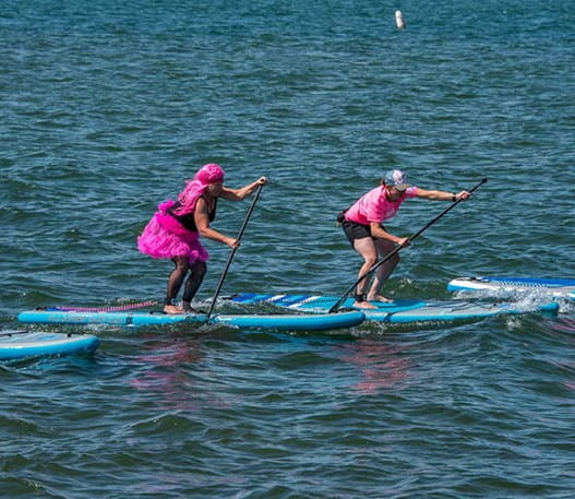 Four people on paddle boards in water wearing pink outfits